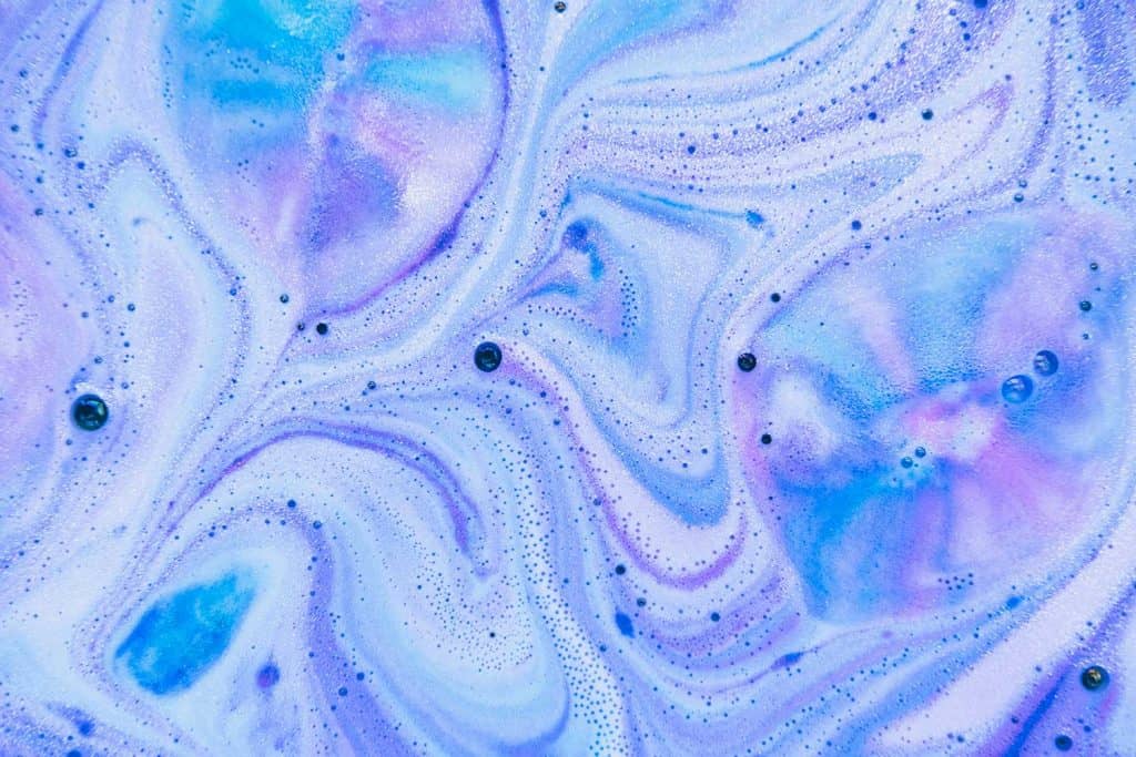 Beautiful bath bomb dissolves in blue, purple and pink colors in the water