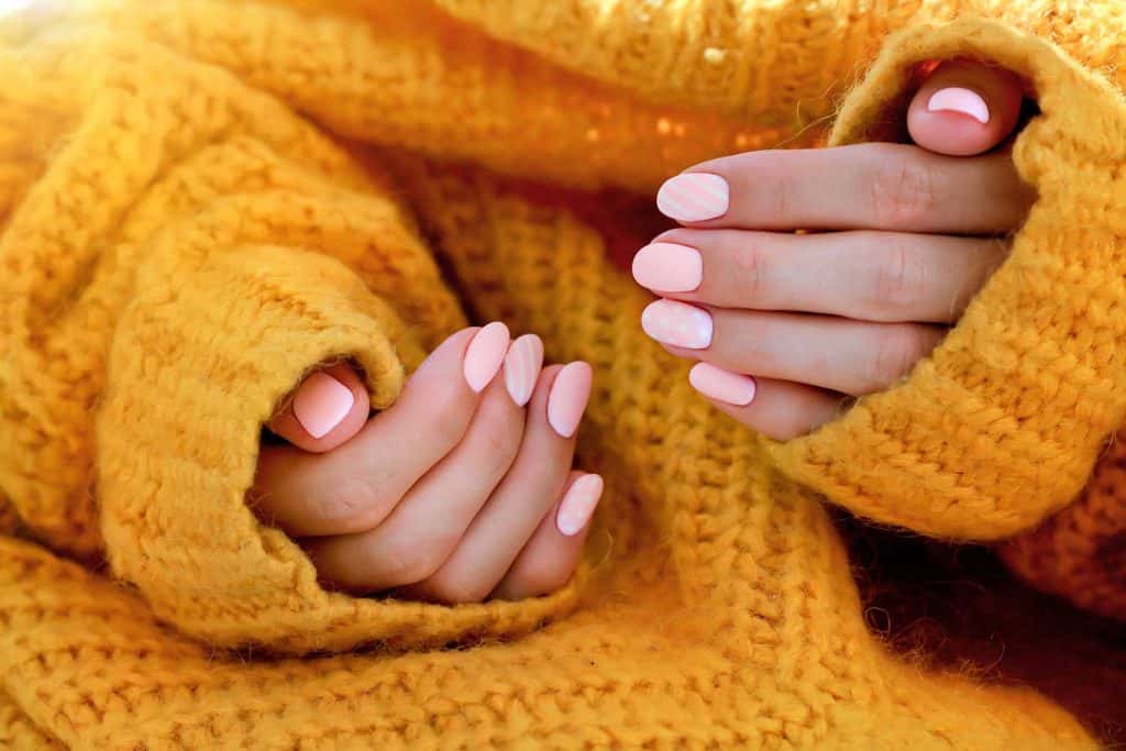 Beautiful female with shaped pink manicure in an orange sweater