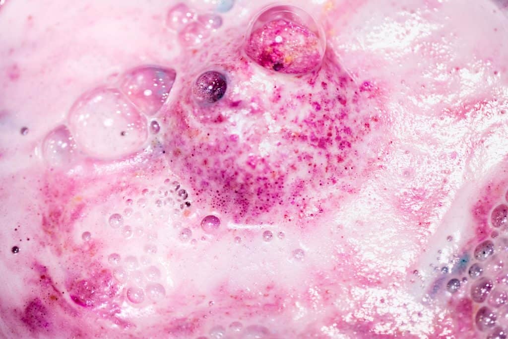 Bright pink colored bath bomb dissolving on the bathtub