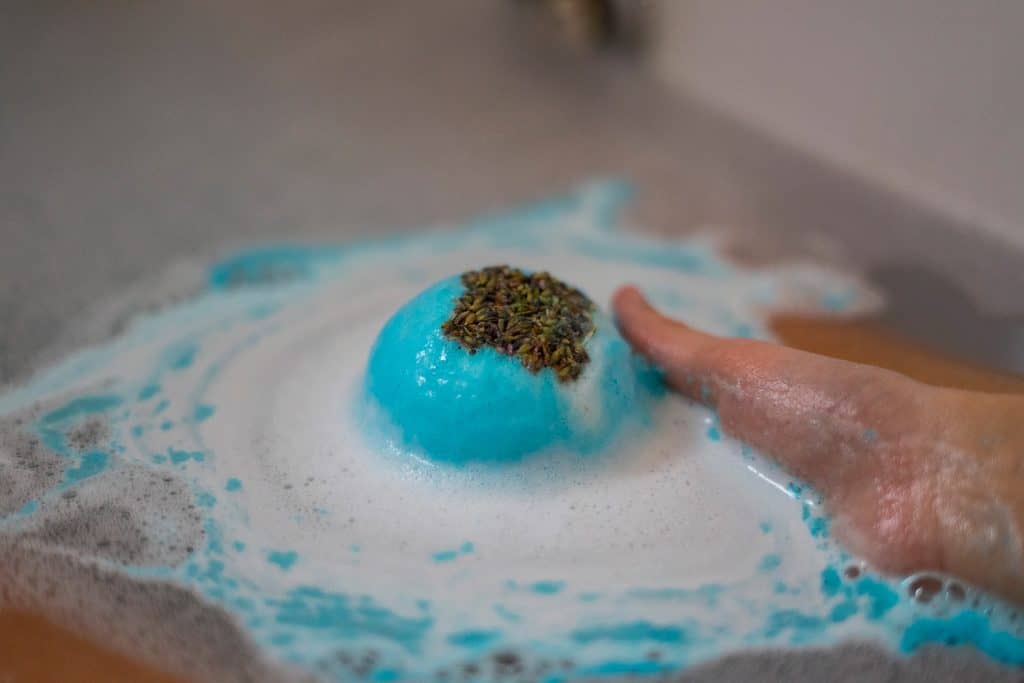 Hand taking a blue bath bomb dissolving in the bathtub