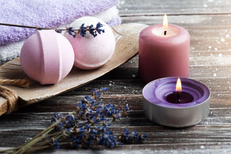 Pink colored bath bombs with a pink candle on the side on top of a wooden table, Can You Use A Bath Bomb In The Shower?