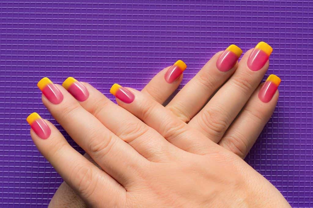 Woman hands with yellow pink square or squoval shaped nails on purple grid