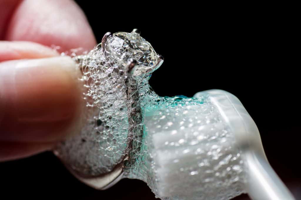 Женские руки чистят бриллиантовое кольцо зубной щеткой и мылом