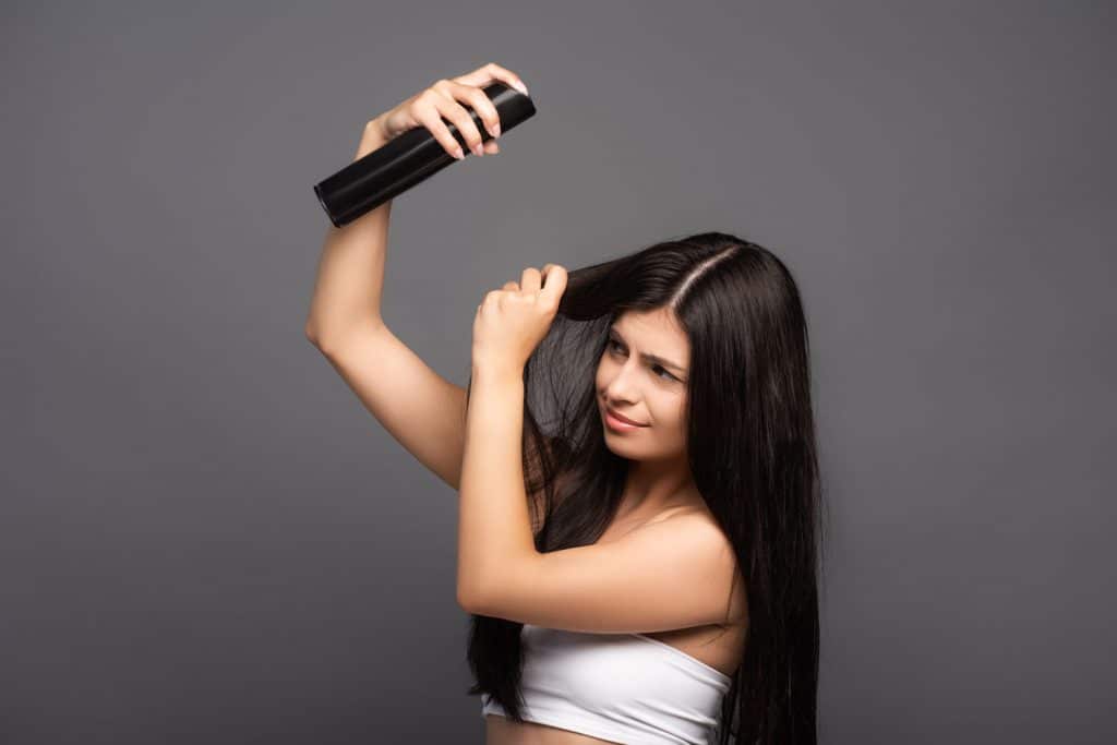 A Latina woman applying hairspray on her hair
