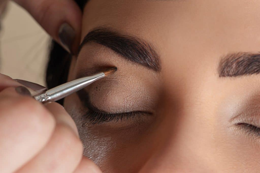 A woman applying brown eyeshadow by her makeup artist