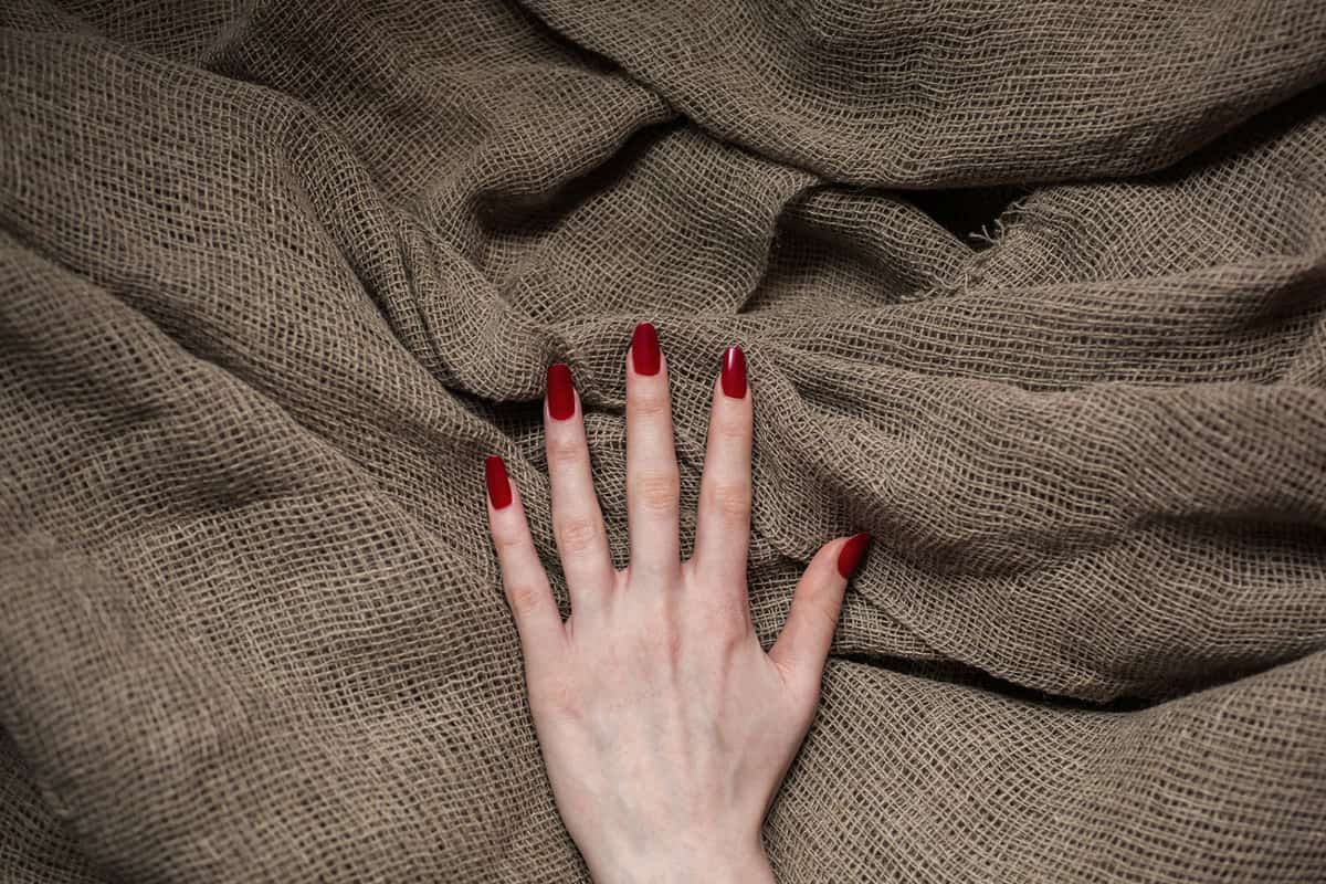 A woman showing her red polished nails on a burlap background