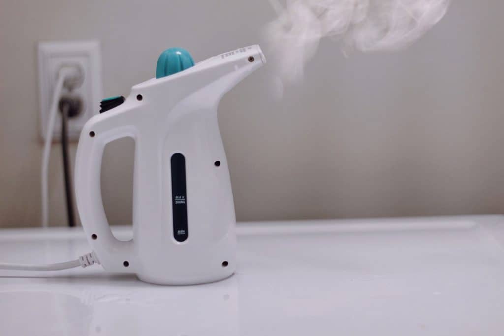An image of a clothes steamer with steam, on the washing machine
