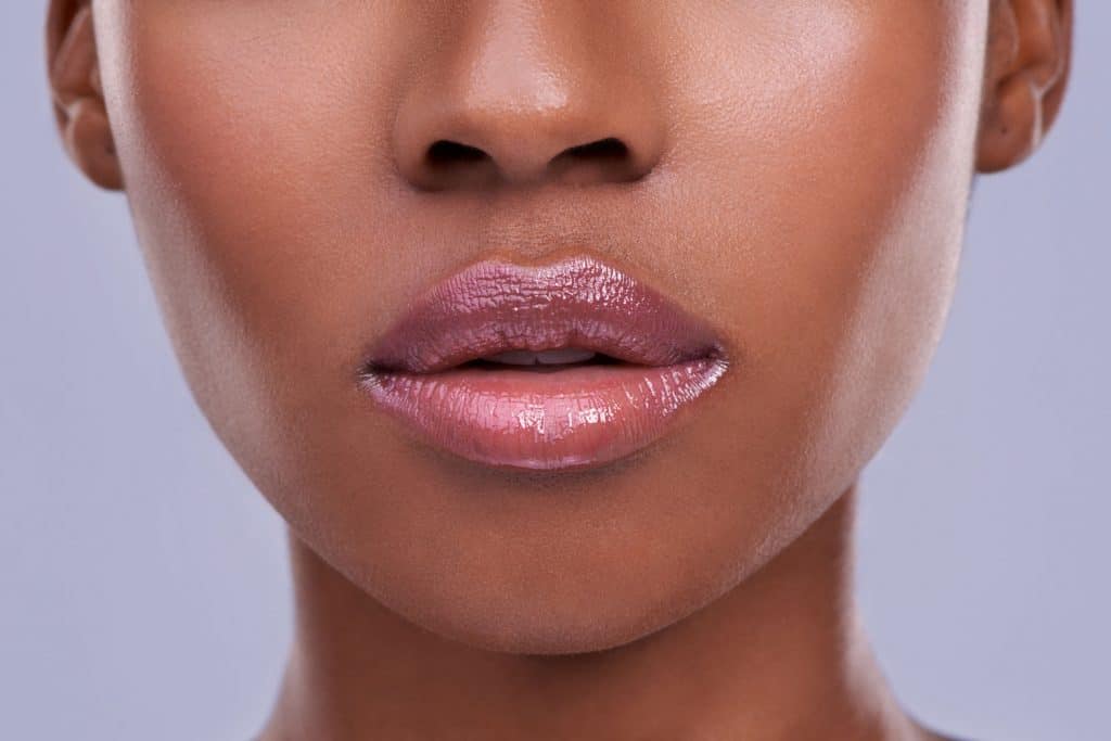 Cropped shot of a young woman's mouth against a purple background, Does Lipstick Fade Your Lip Color?