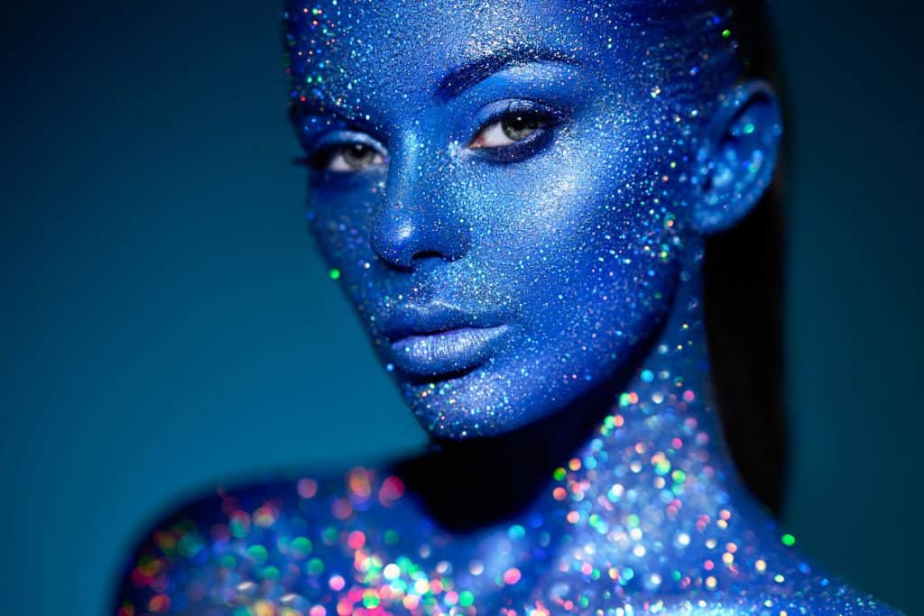 Fashion model woman in blue bright sparkles and neon lights posing in studio, Does Body Glitter Expire? [And How Long Does It Last?]