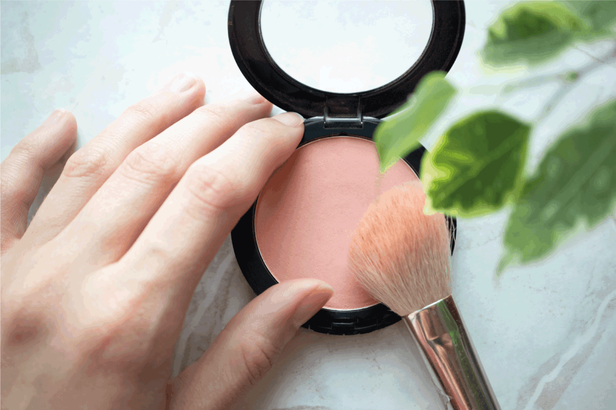 Female hand holding opened blush powder and brush in interior. Top view, Close-up