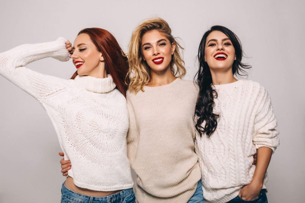 Three gorgeous women wearing sweaters, jeans, and red lipstick