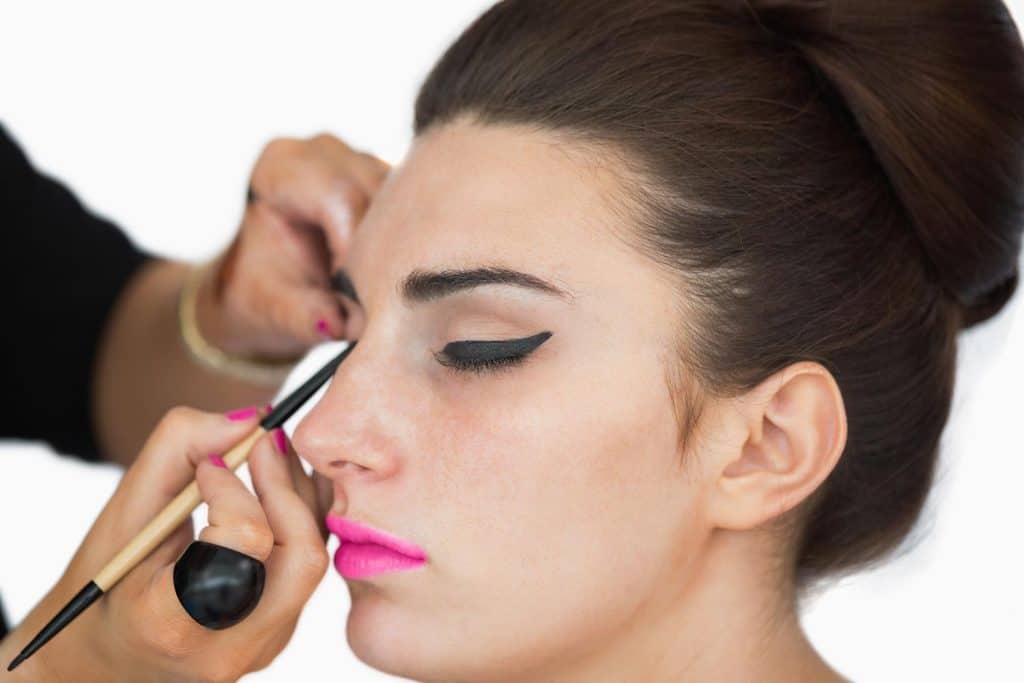 Woman with pink lips getting applied with cat eye makeup