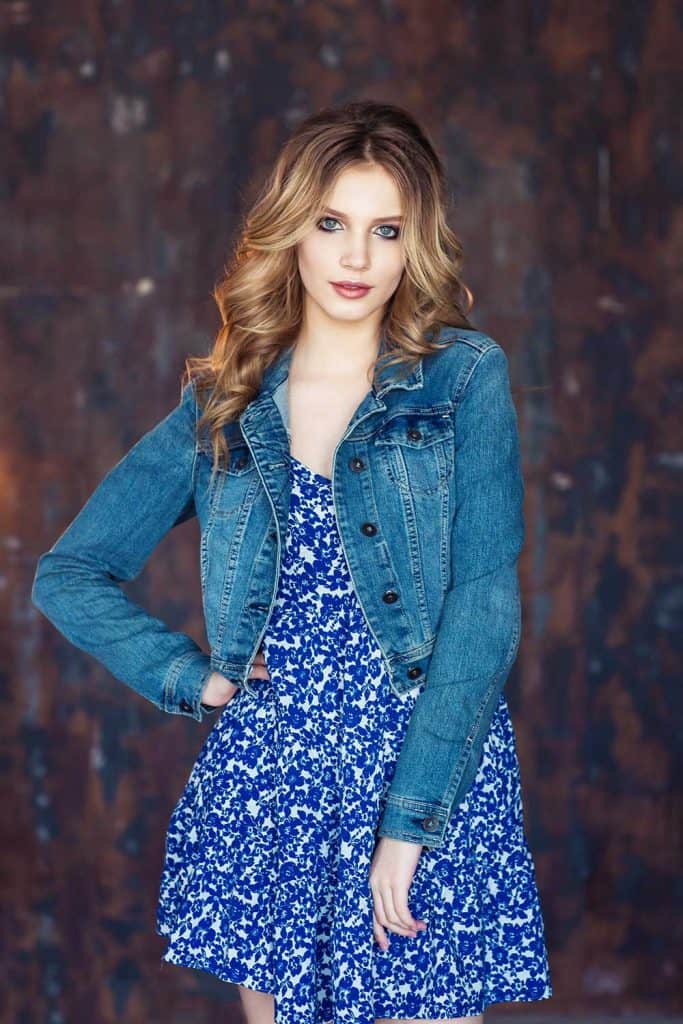 Blonde woman with wavy hair wearing bright blue dress and denim jacket
