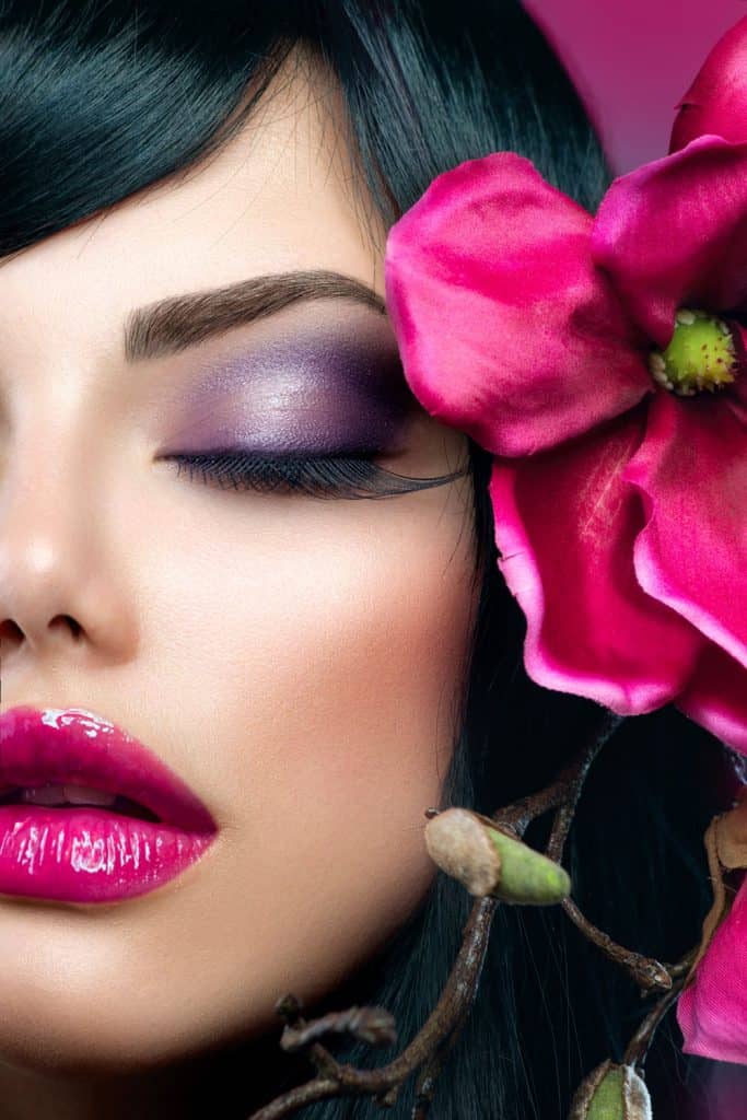 A gorgeous woman wearing dark purple eyeshadow, pink gloss lipstick and a flower