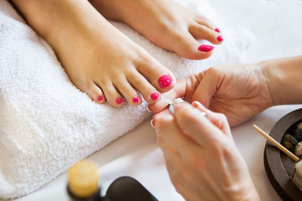 A pedicure artist applying pink nail polish on her clients nail