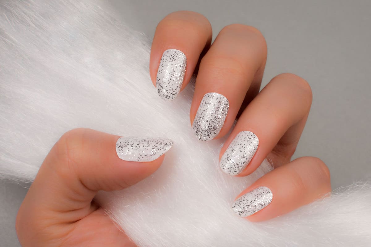 A woman holding furr showing her nails with gray glitter design