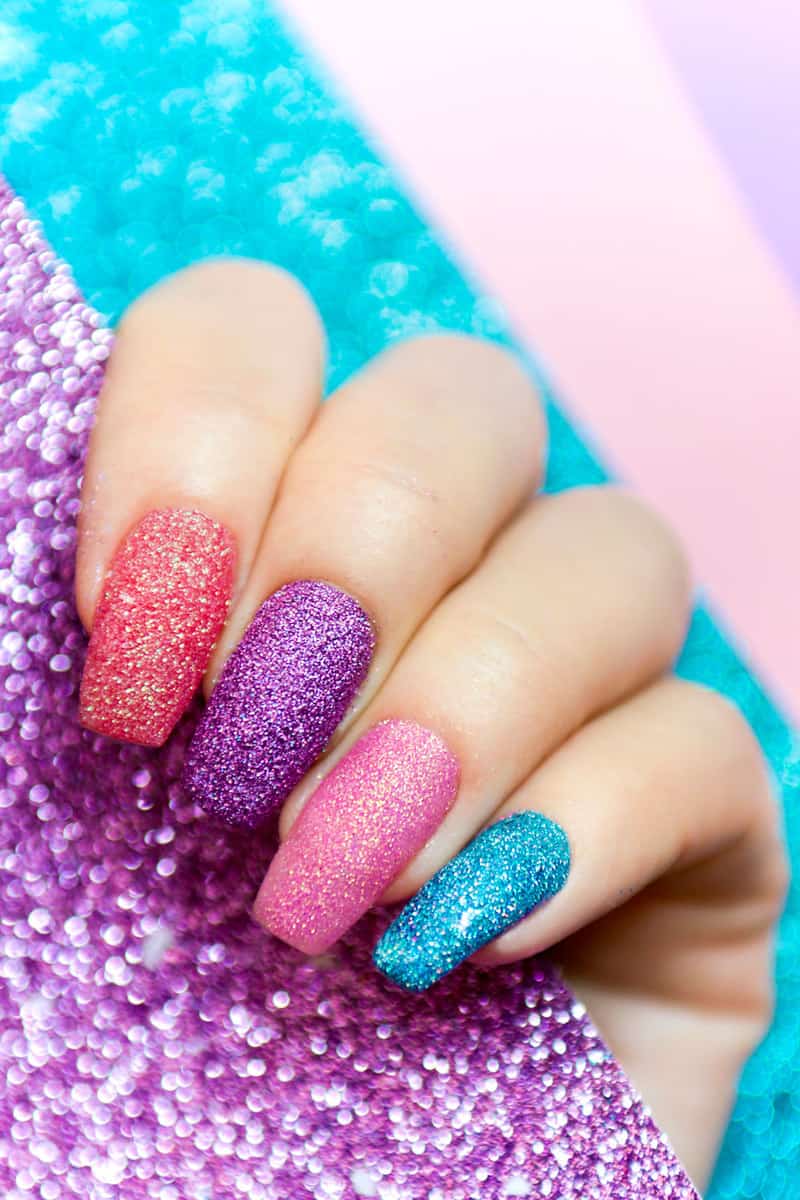 A woman showing her multi-colored glitter finger nail designs