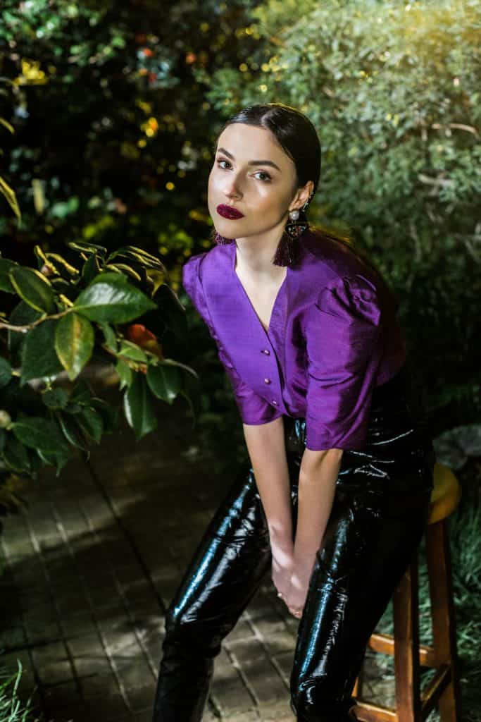 A woman wearing a violet blouse and leather pants on the garden