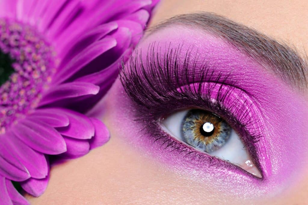 An up close photo of a model wearing light purple eyeshadow and a violet flower