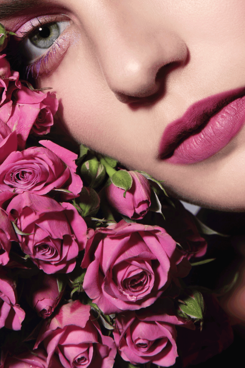 Close-up portrait of young beautiful woman with pink roses and wearing mulberry lipstick