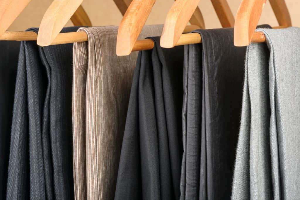 Different types of pants on wooden hangers. Selective focus.