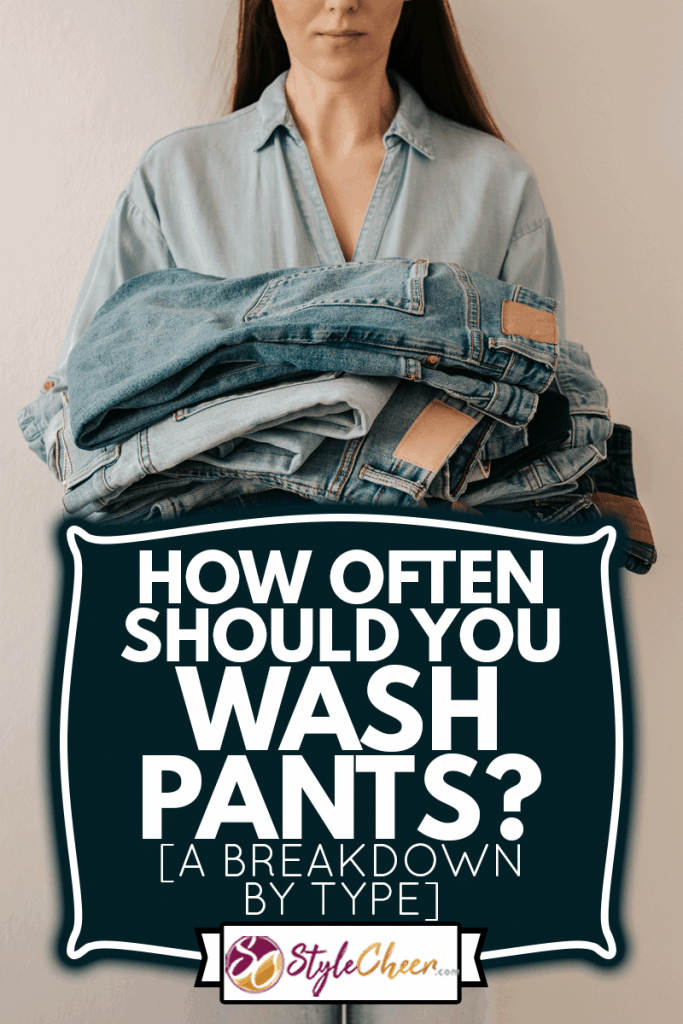 Unrecognizable woman holds stack of lot jeans pants on white background, How Often Should You Wash Pants? [A Breakdown By Type]
