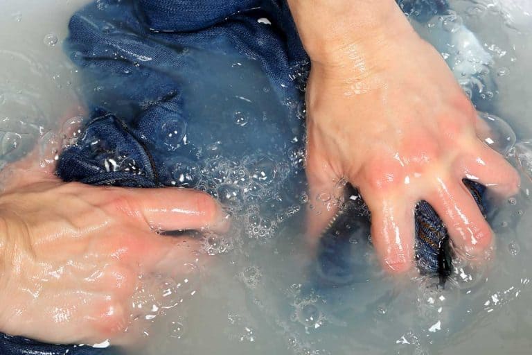 Woman washing a pair of jeans by hand in plastic tub, How To Remove Oil Stains From Jeans