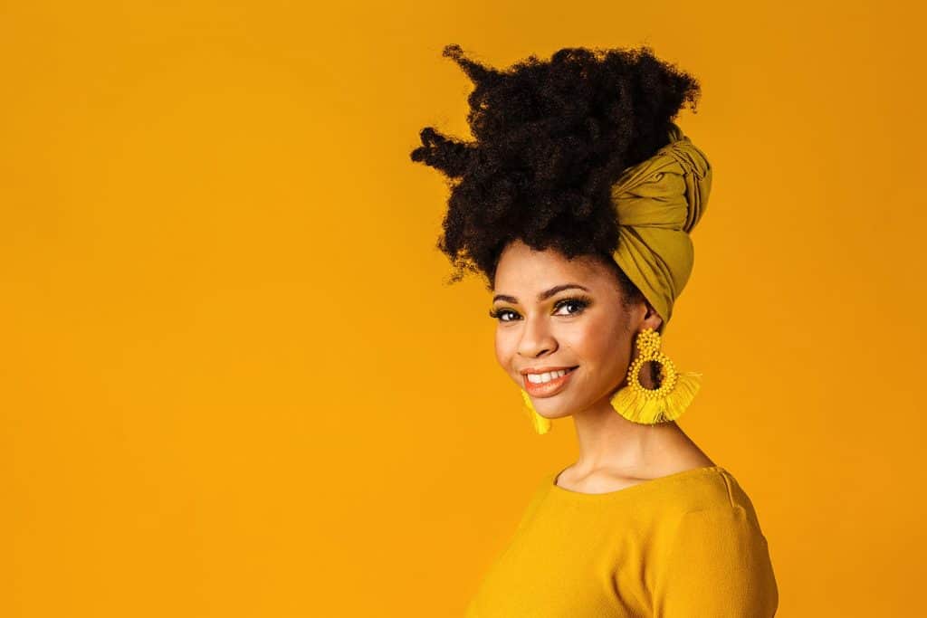 Portrait of a smiling young woman with big yellow tassel beaded earrings and afro hair wrapped with head wrap scarf