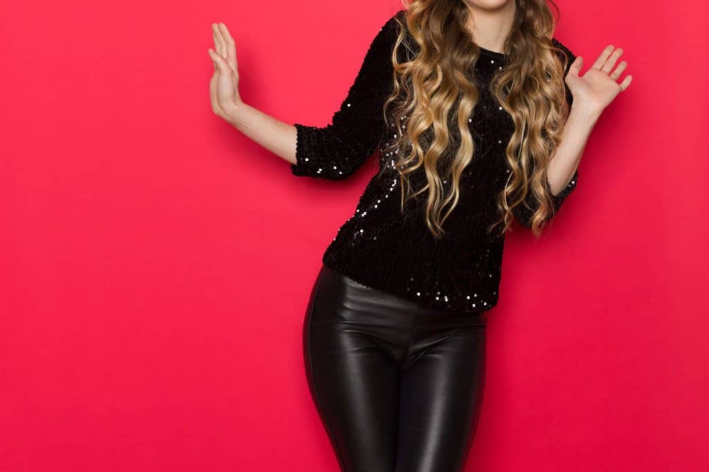 A happy woman wearing leather pants and a black blouse on a red background, How To Keep Leather Pants From Falling Down [Inc. Faux Leather]