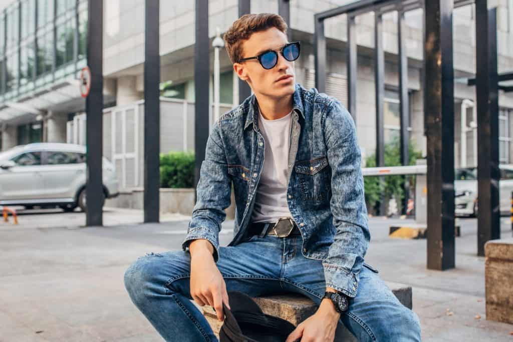 A man wearing a denim jacket and jeans while taking a photo
