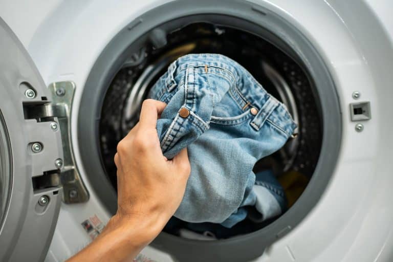 A woman putting her jeans inside the washing machine, Should You Wash Jeans Inside Out?