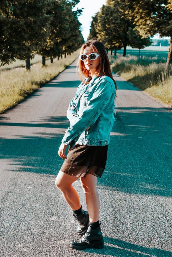 A woman wearing a denim jacket and a mini skirt taking a photograph on the small narrow road