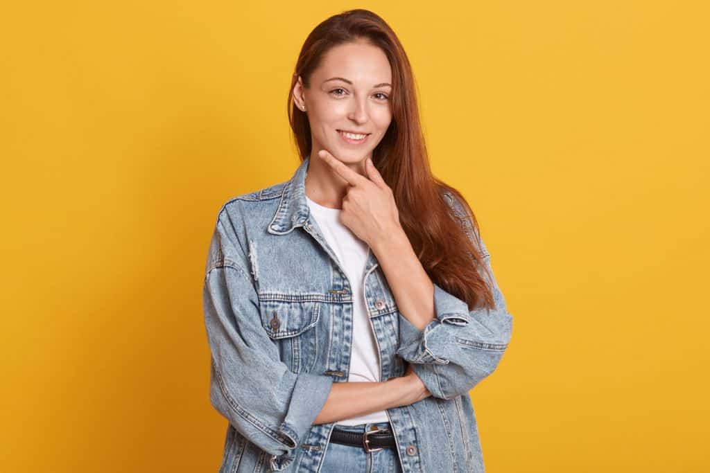 An attractive woman wearing an oversized denim jacket on a yellow background, Should A Denim Jacket Be Tight Or Oversized?