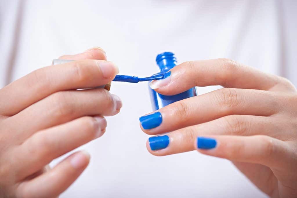 Close-up of woman hands applying blue nail polish on fingernails