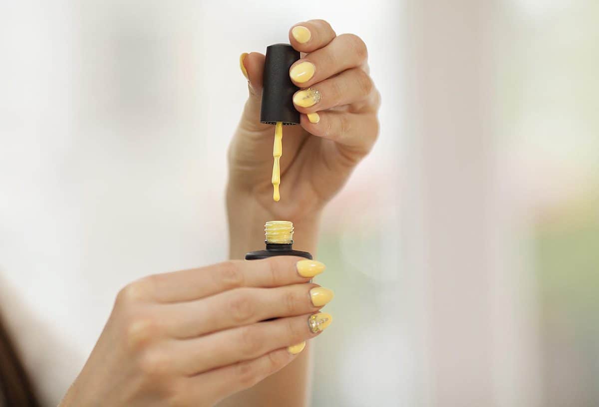 Hands holding yellow nail polish tube and cap with nail brush