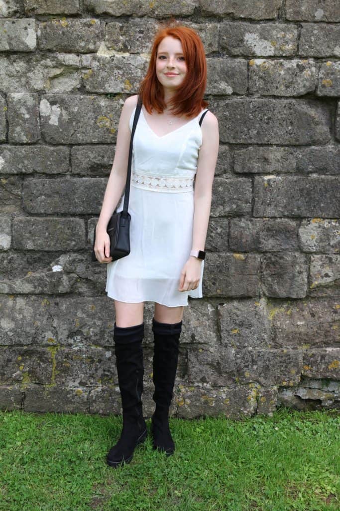 A beautiful red head woman wearing a white dress and black thigh high boots
