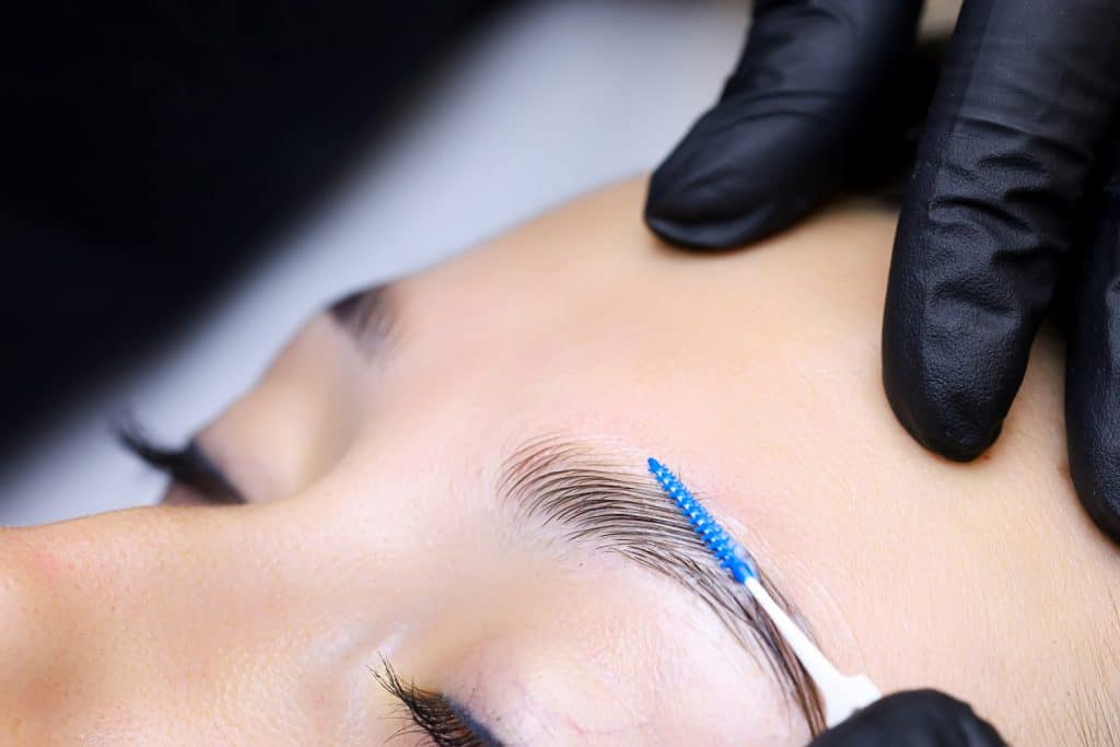 close-up of the master's hands holding a micro brush that combs the eyebrows and models after the eyebrow lamination procedure