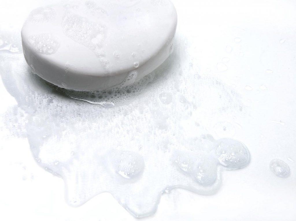 A bar of white soap in a puddle of suds and water