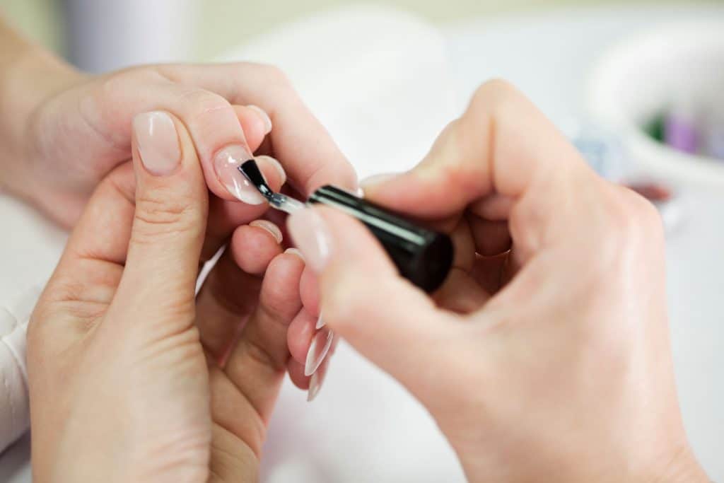 A manicurist applying base coat to her clients nails