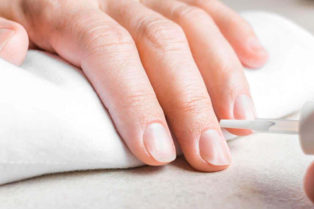 A manicurist applying base coat to her clients nails