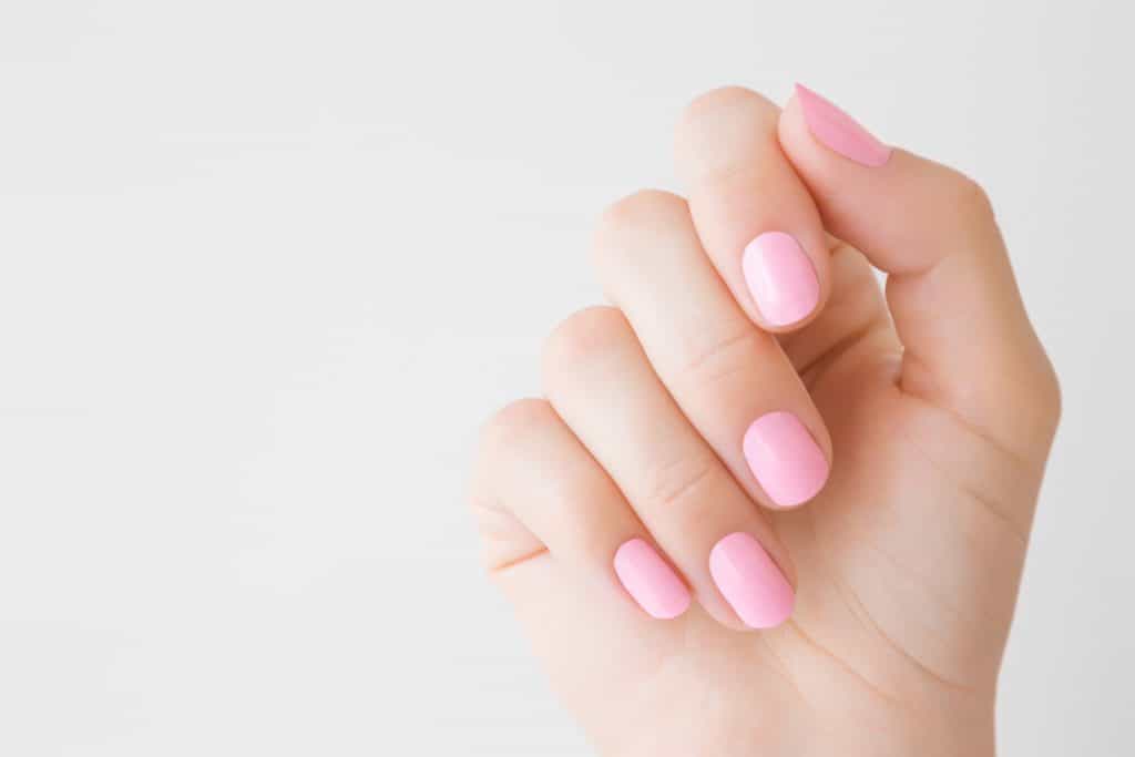 Beautiful groomed woman's hand with pink nails on light gray background. Manicure, pedicure beauty salon concept