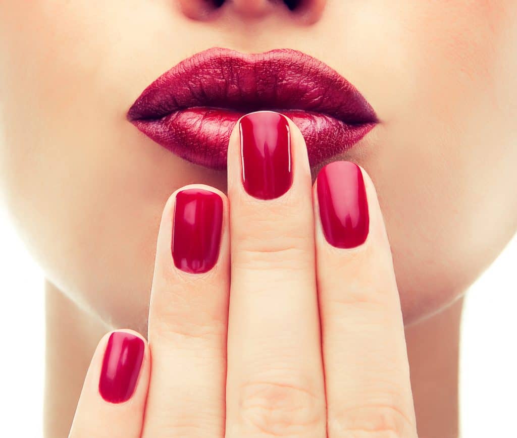 Красивая модель демонстрирует красный маникюр на ногтях.  Красные губы. Роскошный модный стиль, маникюр для ногтей, косметика и макияж.