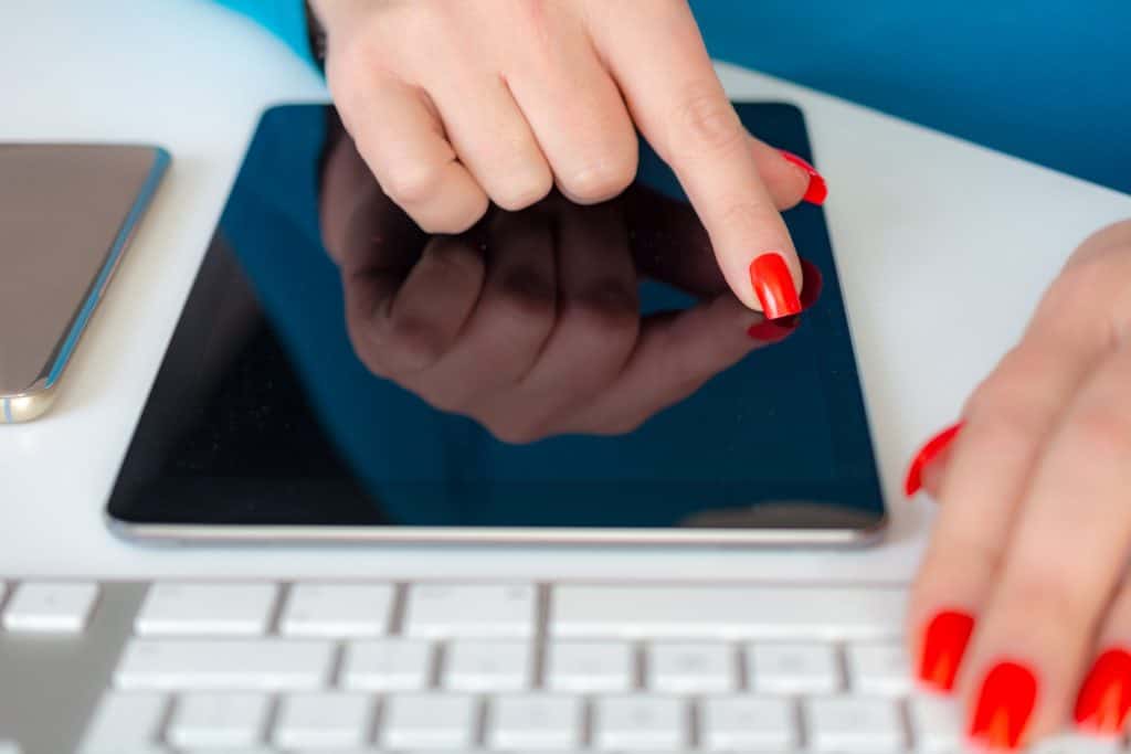 Зрелая женщина работает на своем смартфоне и планшете из розового золота за клавиатурой ПК, зрелая женщина с оранжевыми ногтями