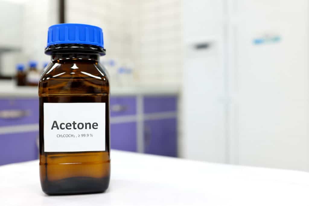 Selective focus of pure acetone solution in brown glass amber bottle inside a chemistry laboratory. White background with copy space.