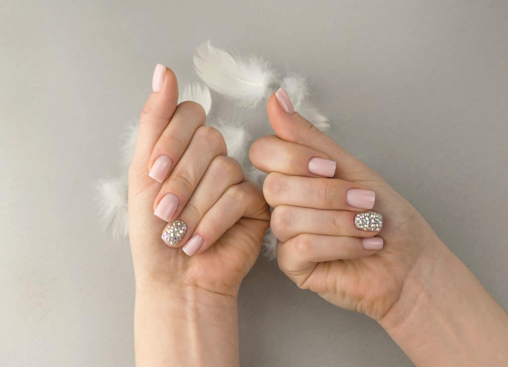 Elegant fashionable women's pink manicure with feathers, square shape of rhinestones