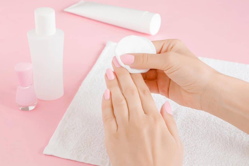 Woman's hand removing pink nail polish with white cotton pad on towel