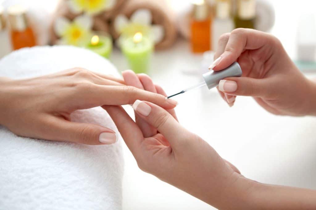 A manicurist putting a colorless top coat on her clients nails