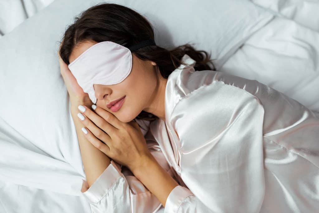 A woman sleeping nicely in her bed wearing a white sleeping mask