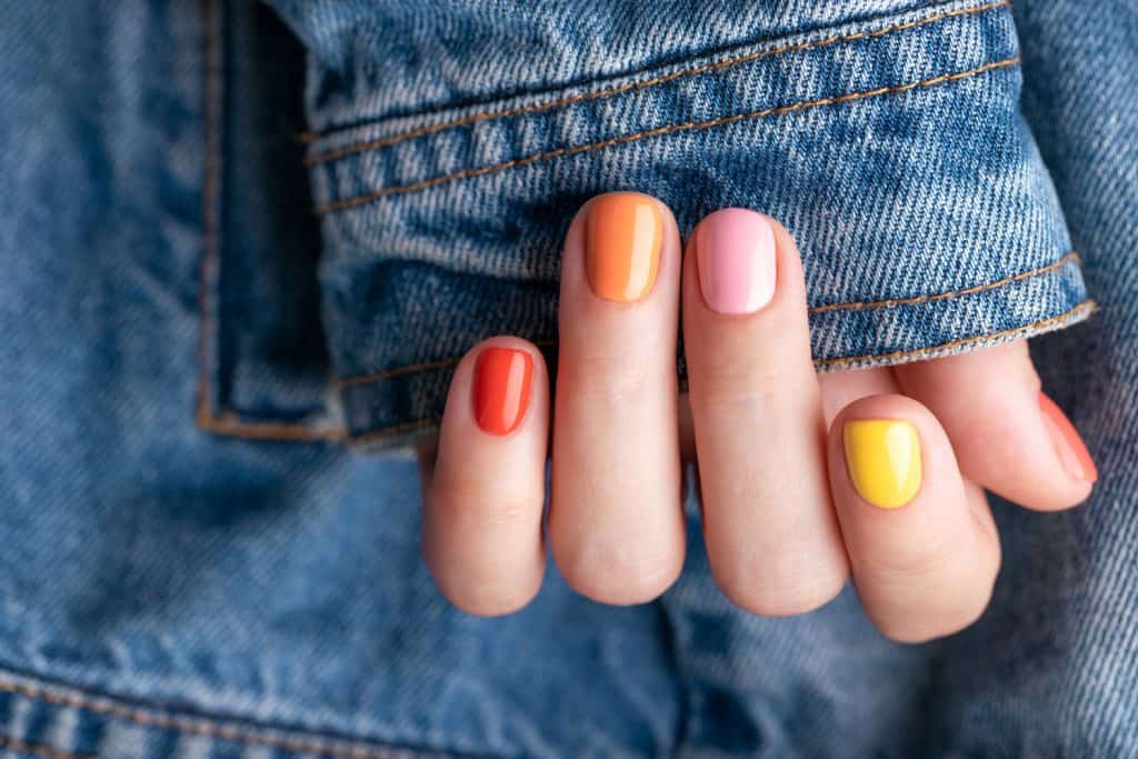 Женская рука с красочным маникюром на фоне джинсовой куртки.
