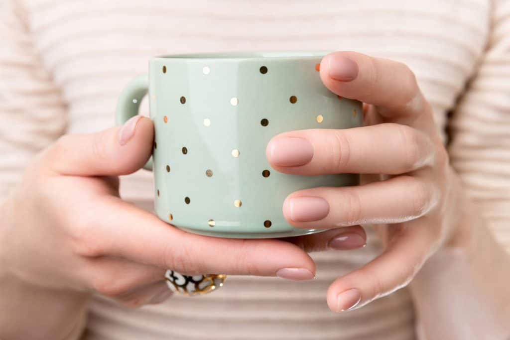 Woman with groomed hands with nude beige pink nail design holding mug